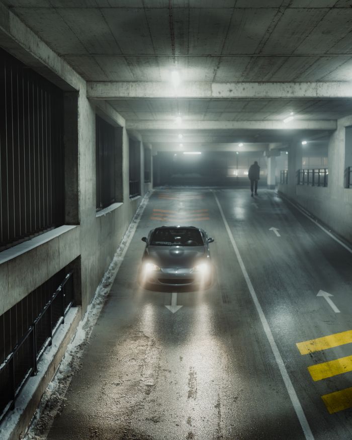 Services A car driving in an illuminated underground parking garage with a person in the distance.